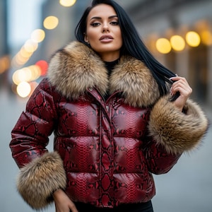 Könnte beinhalten: Rote Steppjacke mit Schlangenmuster, Pelzkragen und Manschetten. Die Jacke hat einen Reißverschluss und ein gestepptes Design. Der Pelzbesatz ist hellbraun und die Jacke scheint aus glänzendem Material gefertigt zu sein.