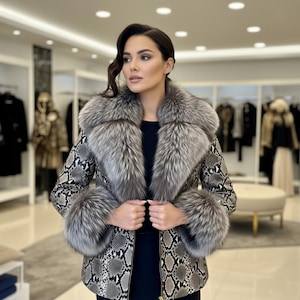 May include: A luxurious jacket with a snakeskin pattern in shades of gray and black. The jacket features a large, fluffy silver fox fur collar and cuffs. The woman in the image is wearing a black top.