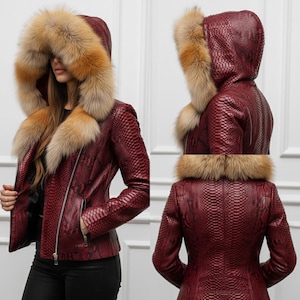 Puede incluir: Chaqueta de cuero burdeos con estampado de piel de serpiente, cierre de cremallera y capucha con ribete de piel marr&oacute;n. La chaqueta tiene una silueta entallada y un bolsillo delantero.