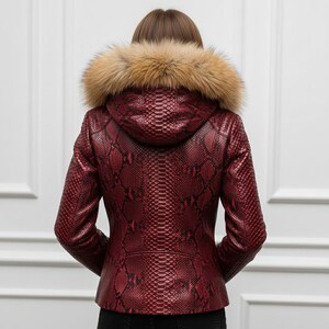 Puede incluir: Chaqueta de cuero roja con estampado de piel de serpiente y capucha con ribete de piel. La chaqueta tiene una silueta entallada y cierre de cremallera. El ribete de piel es de color marr&oacute;n claro. Prenda de abrigo elegante.