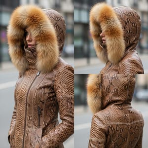 May include: A brown snakeskin-effect jacket featuring a large hood trimmed with tan fur. The jacket has a zip closure and a high collar. The hood frames the face, and the fur adds a luxurious touch. The jacket is a stylish outerwear piece.