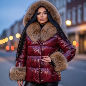 Könnte beinhalten: Burgunderfarbene Pufferjacke mit Schlangenmuster, mit fellgefütterter Kapuze, Kragen und Manschetten. Die Jacke hat ein glänzendes Finish und ein gestepptes Design. Der Pelzbesatz ist hellbraun. Die Jacke ist zugeknöpft.