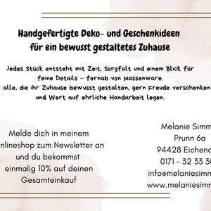 May include: A white informational card with brown border lines and text in German. The text reads: Handgefertigte Deko- und Geschenkideen f&uuml;r ein bewusst gestaltetes Zuhause. Jedes St&uuml;ck entsteht mit Zeit, Sorgfalt und einem Blick f&uuml;r feine Details &ndash; fernab von Massenware. F&uuml;r alle, die ihr Zuhause bewusst gestalten, gern Freude verschenken und Wert auf ehrliche Handarbeit legen. Melde dich in meinem Onlineshop zum Newsletter an und du bekommst einmalig 10% auf deinen Gesamteinkauf. Melanie Simmel, Prunn 6a, 94428 Eichendorf, 0171 - 32 33 304, info@melaniesimmel.de, www.melaniesimmel.de.