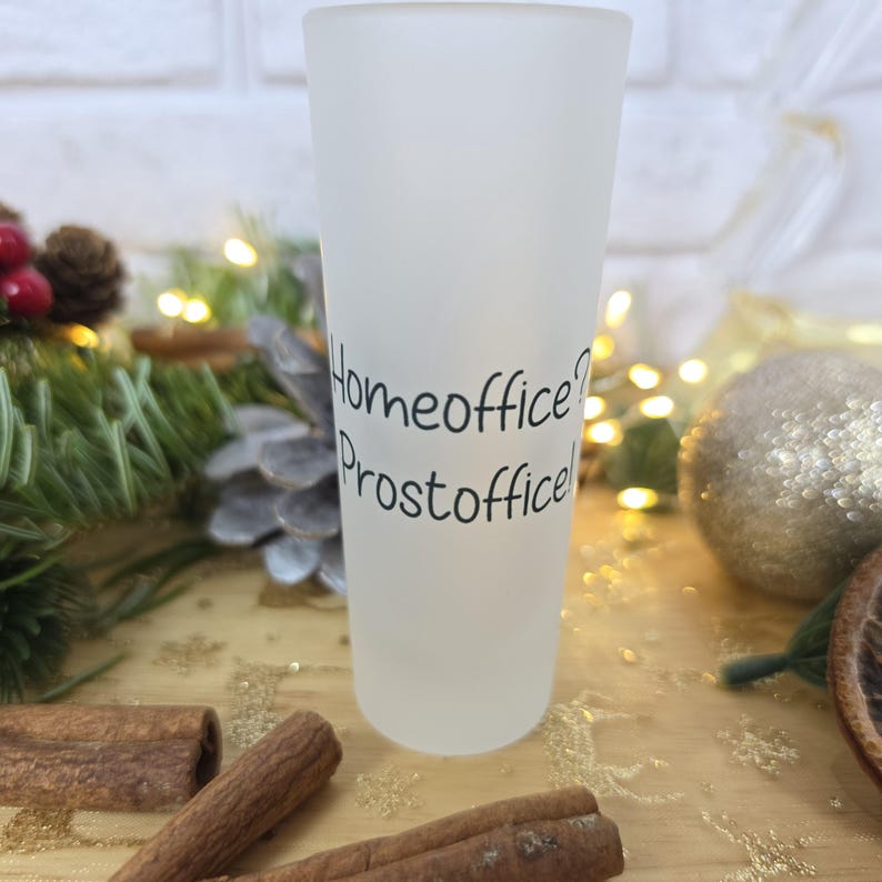 May include: A tall, frosted glass shot glass featuring the black printed text Homeoffice? Prostoffice! The glass has a cylindrical shape with a smooth, matte finish and a clear rim at the top, standing upright as a single drinking vessel.