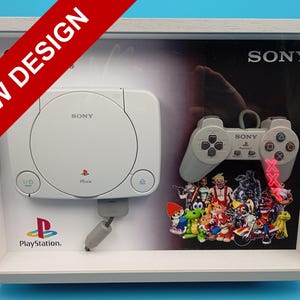 Puede incluir: Una pantalla enmarcada con una consola y un mando de PlayStation blancos, con el logotipo de Sony. La pantalla incluye una colección de pegatinas de personajes coloridos y el texto "NEW DESIGN" en una pancarta diagonal roja.