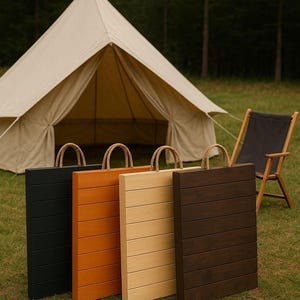Puede incluir: Cuatro bandejas de madera para servir en negro, naranja, beige y marrón oscuro, cada una con un asa de cuerda. Una tienda de campaña de lona y una silla plegable en el fondo, sugieren un tema al aire libre.
