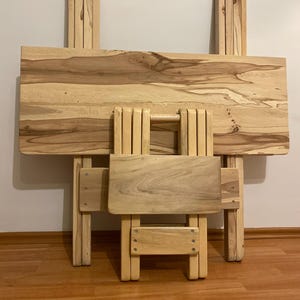Puede incluir: Un juego de mesa y silla de madera plegada. La mesa tiene una tapa rectangular y patas plegables. La silla también es de madera y tiene un asiento y respaldo pequeños. El conjunto es de color marrón claro y parece nuevo. La mesa mide unos 76 cm.