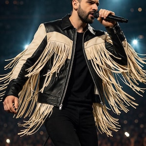 May include: Black leather jacket with cream-colored panels and long fringe detailing. The jacket has a zipper closure and is worn with black pants. The overall style is a modern take on a Western aesthetic.