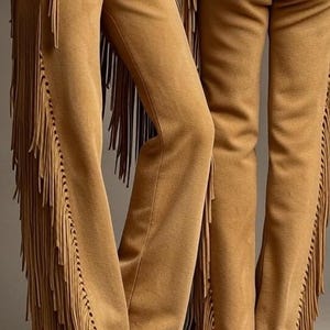 Peut inclure: Pantalon en daim beige avec des franges décoratives sur les côtés. Le pantalon a une taille haute avec des boutons argentés. Le pantalon est d'inspiration western, adapté à un costume ou à une déclaration de mode unique.