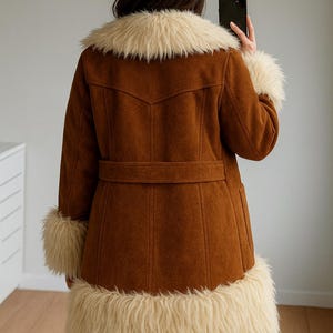 May include: Brown suede coat with cream faux fur trim on the collar, cuffs, and hem. The coat has a belt at the waist and a classic design. A stylish outerwear piece.