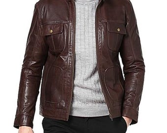 May include: A brown leather jacket with a stand-up collar and two chest pockets. The jacket has a zipper closure and two lower pockets. The model is wearing a gray sweater underneath the jacket.