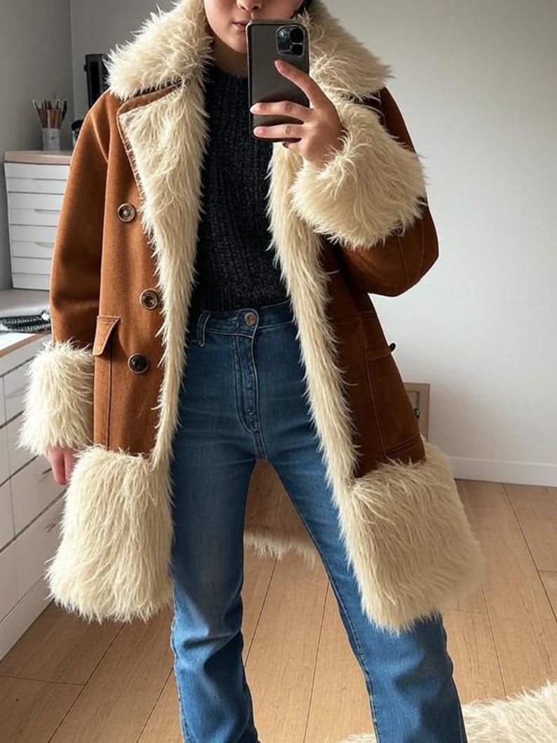 May include: A brown suede coat with cream faux fur trim on the collar, cuffs, and front. The coat features a double-breasted design with large buttons. It is worn with blue denim jeans.