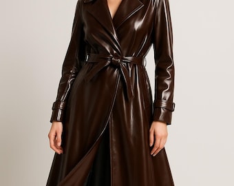 May include: A long, brown leather trench coat with a belted waist and a classic lapel collar. The coat is knee-length and has long sleeves with buttoned cuffs. The coat is open in the front, revealing a glimpse of the lining.