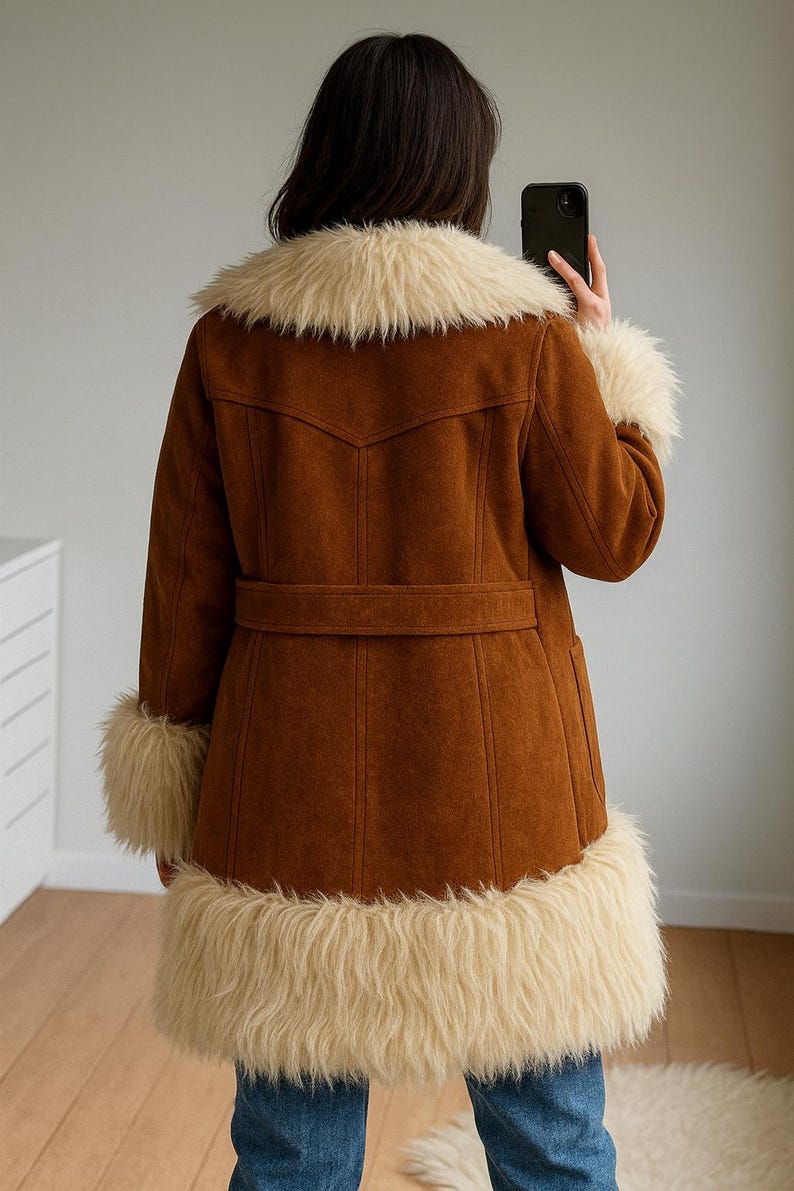 May include: Brown suede coat with cream faux fur trim on the collar, cuffs, and hem. The coat has a belt at the waist and a classic design. A stylish outerwear piece.