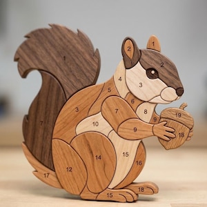 May include: A wooden squirrel jigsaw puzzle with numbered pieces. The squirrel holds an acorn. The puzzle is made of various shades of brown wood, with a dark brown tail and head, and lighter brown body pieces.