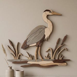 Könnte beinhalten: Wandkunst aus Holz, die einen Reiher in einem Sumpf darstellt. Der Reiher ist aus verschiedenen Holztönen gefertigt, mit einem hellbraunen Körper, grauen Flügeln und einem dunkelbraunen Kopf. Schilf und Wasserpflanzen sind ebenfalls aus Holz gefertigt. Das Kunstwerk ist mit "Wildwood Artisans" signiert.