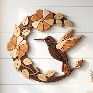 May include: A crescent-shaped wooden wall art piece featuring a hummingbird in flight surrounded by flowers and leaves. The design is crafted from various shades of natural wood, ranging from light tan to dark brown, creating a layered effect.