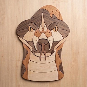 May include: Wooden snake head sculpture with a detailed design. The sculpture features a variety of wood tones, including light and dark browns, and tan. The snake's eyes are yellow, and its fangs are visible. The sculpture is mounted on a light wood surface.