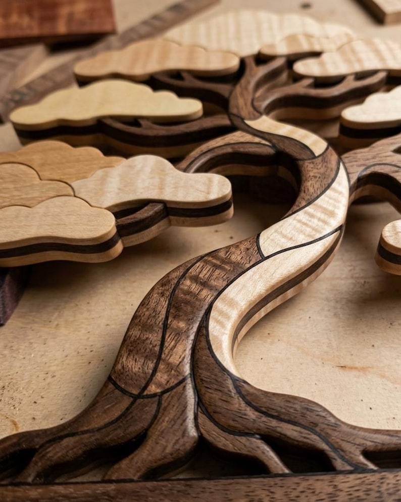 May include: A wooden wall art piece shaped like a bonsai tree, constructed from contrasting light and dark wood segments. The design features layered, cloud-like foliage sections and a curved, textured trunk with visible wood grain patterns.