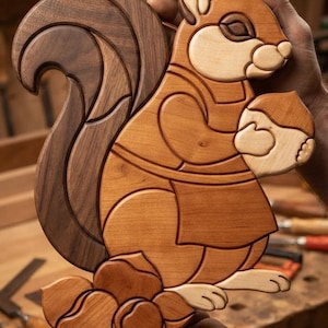 May include: A handcrafted wooden intarsia wall art piece depicting a squirrel wearing a chef hat and apron, holding an acorn. The design features contrasting light and dark wood tones, with a large bushy tail and several acorns at the base.
