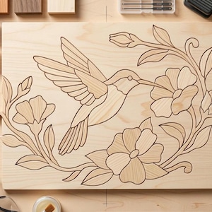 May include: A rectangular light-colored wooden board featuring a dark laser-engraved design of a hummingbird in flight surrounded by floral vines and blossoms. The wood grain is visible throughout the surface, highlighting the detailed line art.