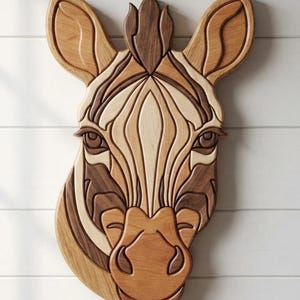 Può includere: Una scultura da parete a forma di testa di zebra realizzata con diverse tonalità di legno naturale. Il pezzo presenta complessi segmenti stratificati in toni marrone chiaro, medio e scuro, che formano i tratti del viso, le orecchie e la criniera.