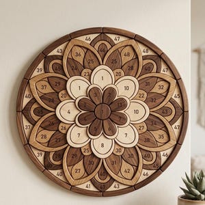 May include: A wooden mandala wall art piece with a floral design. The circular artwork features a series of interlocking wooden pieces in varying shades of brown and natural wood, with numbers on each piece. The diameter is approximately 24 inches.