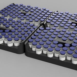 Op de afbeelding: Twee zwarte rechthoekige trays met een grote hoeveelheid kleine doorzichtige glazen flesjes met donkerblauwe doppen. De flesjes zijn in een rasterpatroon geplaatst in de gevormde uitsparingen van de trays, die zijn voorzien van geïntegreerde handgrepen.