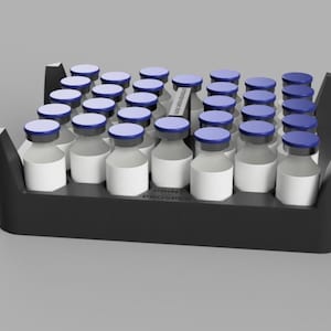 Può includere: Un vassoio nero contiene numerosi piccoli flaconi di vetro con etichette bianche e tappi blu. I flaconi sono disposti in file. Il vassoio ha una forma rettangolare con i lati rialzati. Lo sfondo è di colore grigio uniforme.