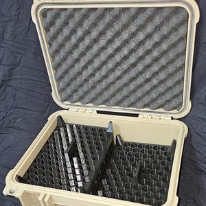 May include: A tan-coloured, hard-shell case, open to reveal a black interior. The case has a handle and latches for secure closure. The interior features black foam padding and compartments for organising items. Designed for protection and storage.