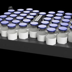 Può includere: Un vassoio nero pieno di numerosi piccoli flaconi di vetro. Ogni flacone ha un'etichetta bianca e un tappo blu. I flaconi sono disposti ordinatamente all'interno del vassoio, che ha i lati rialzati. Lo sfondo è nero.