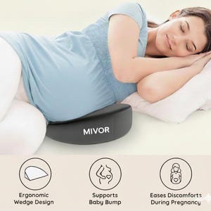 May include: A black ergonomic wedge pillow with the brand name "MIVOR" in white text. The pillow is designed to support the baby bump and ease discomfort during pregnancy. The image shows a person resting on the pillow.
