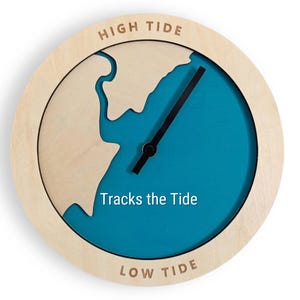 Può includere: Un orologio a marea rotondo in legno chiaro con un centro blu turchese. Il quadrante presenta un contorno di mappa e lancette nere. Le parole "HIGH TIDE" e "LOW TIDE" sono in alto e in basso, con "Tracks the Tide" al centro.