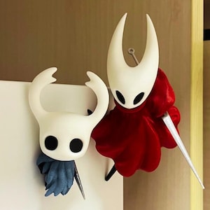 May include: Two white figurines with black eyes and horns. One wears a red cape and holds a silver sword. The other has a blue scarf and a silver sword. The figurines are likely from a video game.
