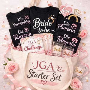 Könnte beinhalten: Eine beigefarbene Tragetasche gefüllt mit schwarzen T-Shirts, Schnapsgläsern und Karten. Die Shirts haben weißen und rosa Text, darunter "Bride to be" und "Die Tänzerin". Rosa Rosen und Bänder umgeben die Tasche, mit einem herzförmigen "Love"-Schild.