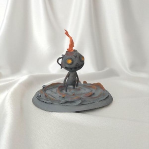 May include: A grey figurine of a creature with a flame emerging from its head. The figure has a round head with two yellow eyes and small arms and legs. It stands on a grey circular base with orange accents.