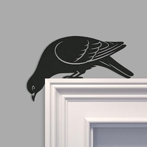 May include: A black metal dove silhouette, positioned on a white surface. The bird is shown with its head lowered, as if feeding. The design includes detailed wing and tail feather outlines, creating a decorative accent.