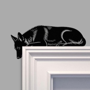 Puede incluir: Una silueta negra de un perro acostado, con detalles blancos grabados. El perro descansa sobre una superficie rectangular blanca. El fondo es de color gris sólido.