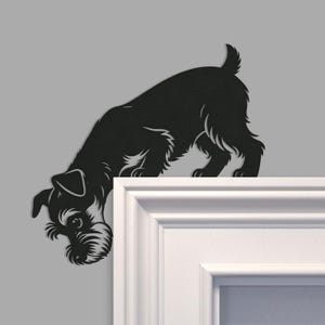 May include: A black metal wall art piece shaped like a terrier dog silhouette, designed to be mounted on the corner of a door frame. The dog is depicted in a downward-looking pose with detailed fur textures around the face and ears.