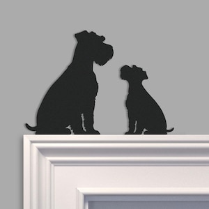 Op de afbeelding: Zwart silhouet van twee honden, een volwassen hond en een puppy, die naast elkaar zitten. De honden staan op een witte richel tegen een grijze achtergrond. De honden zijn gedetailleerd en het ontwerp is minimalistisch.