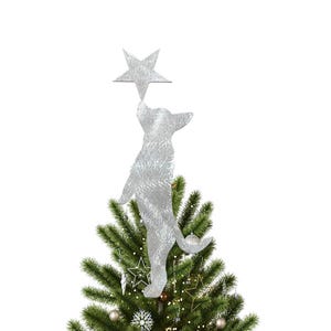 Puede incluir: Un adorno plateado con forma de gato y purpurina para la parte superior del árbol de Navidad que alcanza una estrella plateada con purpurina. El gato está de pie sobre un árbol de Navidad verde decorado con adornos y luces. Una decoración festiva.