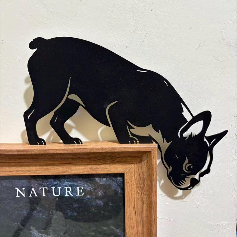 Op de afbeelding: Een zwart-wit silhouet van een Boston Terrier, alsof hij snuffelt, is gemonteerd op een houten frame. Het woord "NATURE" is zichtbaar op het ingelijste kunstwerk. De vorm van de hond is uitgesneden, waardoor een decoratief accent ontstaat.