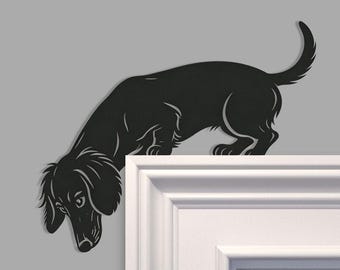 以下が含まれることがあります： コーナーに取り付けるように設計された、長毛のダックスフントの黒い金属製シルエット。犬は頭を床に向けて下を向いた姿勢で描かれており、耳と尻尾に詳細な切り抜きが施されています。