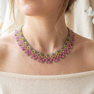 May include: A colourful beaded necklace with a geometric pattern. The necklace features pink, yellow, and grey beads in a repeating diamond design. The necklace is worn around the neck.
