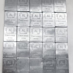 Könnte beinhalten: Eine Ansammlung rechteckiger Aluminiumbarren, jeweils mit "AL", "1 Troy Ounce" und "999 Fine Aluminium" graviert. Die Barren sind in einem Raster angeordnet und zeigen eine metallisch silberne Farbe und das Periodensymbol für Aluminium.
