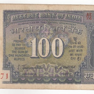 May include: A vintage 100 Indian Rupee banknote featuring the Lion Capital of Ashoka emblem on the right side. The bill displays the text Reserve Bank of India, One Hundred Rupees, and the serial number AE 74 626871 in red ink on the front.