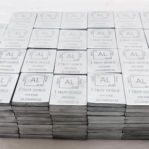 Może przedstawiać: Stosy prostokątnych, srebrnych sztabek aluminium. Każda sztabka jest oznaczona symbolem "AL", "1 Troy Ounce" i "999 Fine Aluminium". Sztabki są starannie ułożone.