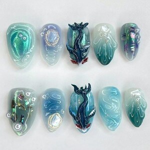 May include: A set of ten almond-shaped artificial nails with intricate designs. The nails feature a variety of colors, including iridescent green, blue, and white. Some nails have 3D embellishments, while others showcase detailed aquatic-themed artwork.