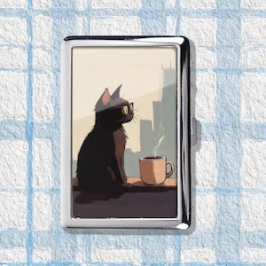 Może przedstawiać: Srebrne metalowe etui na papierosy z ilustracją czarnego kota w okularach przeciwsłonecznych, siedzącego przy oknie z filiżanką kawy. Tło przedstawia panoramę miasta.