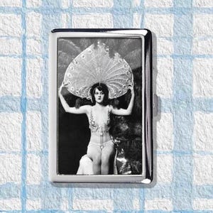 May include: A silver cigarette case featuring a black and white image of a woman in a costume with a large feathered headdress. The image is framed within the rectangular case, which has a shiny, reflective surface.